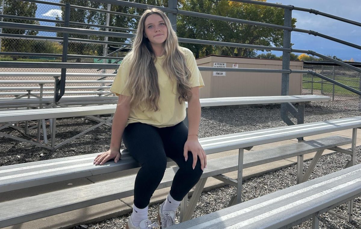 Photo of Lexi Trottier standing on the field she played on this season, and the bleachers near the playing field.